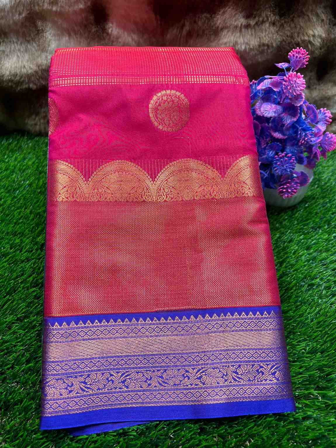 Pink saree with gold and blue border on a green grass background