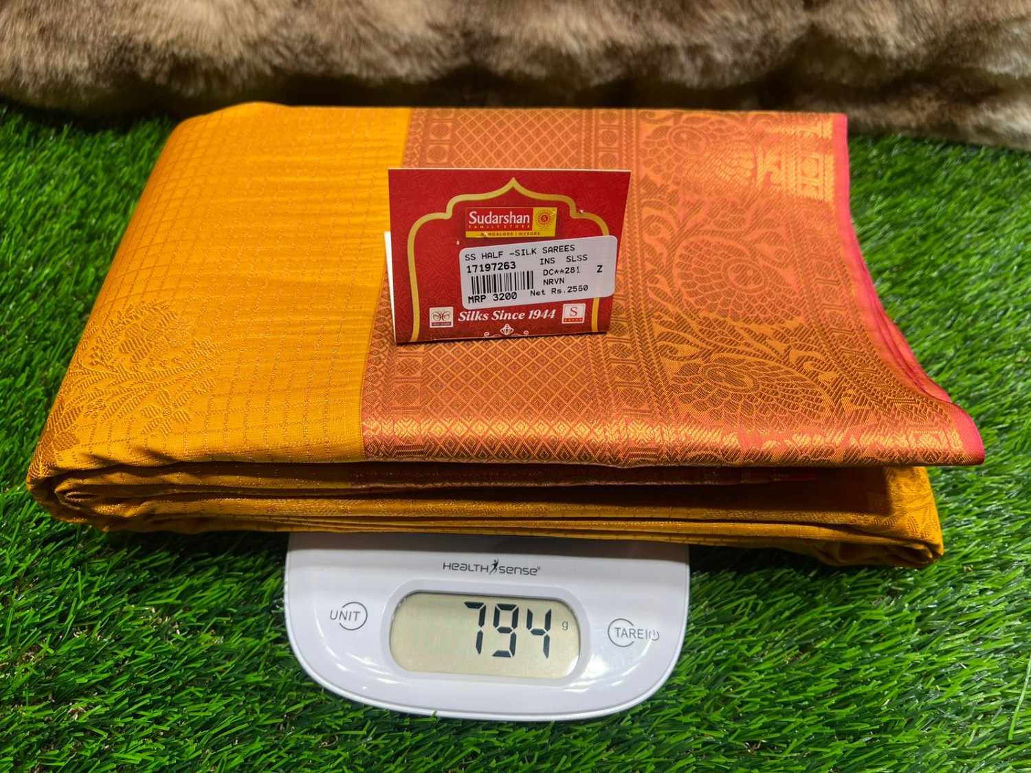 Folded orange and red fabric with a label on top of a digital scale on grass.