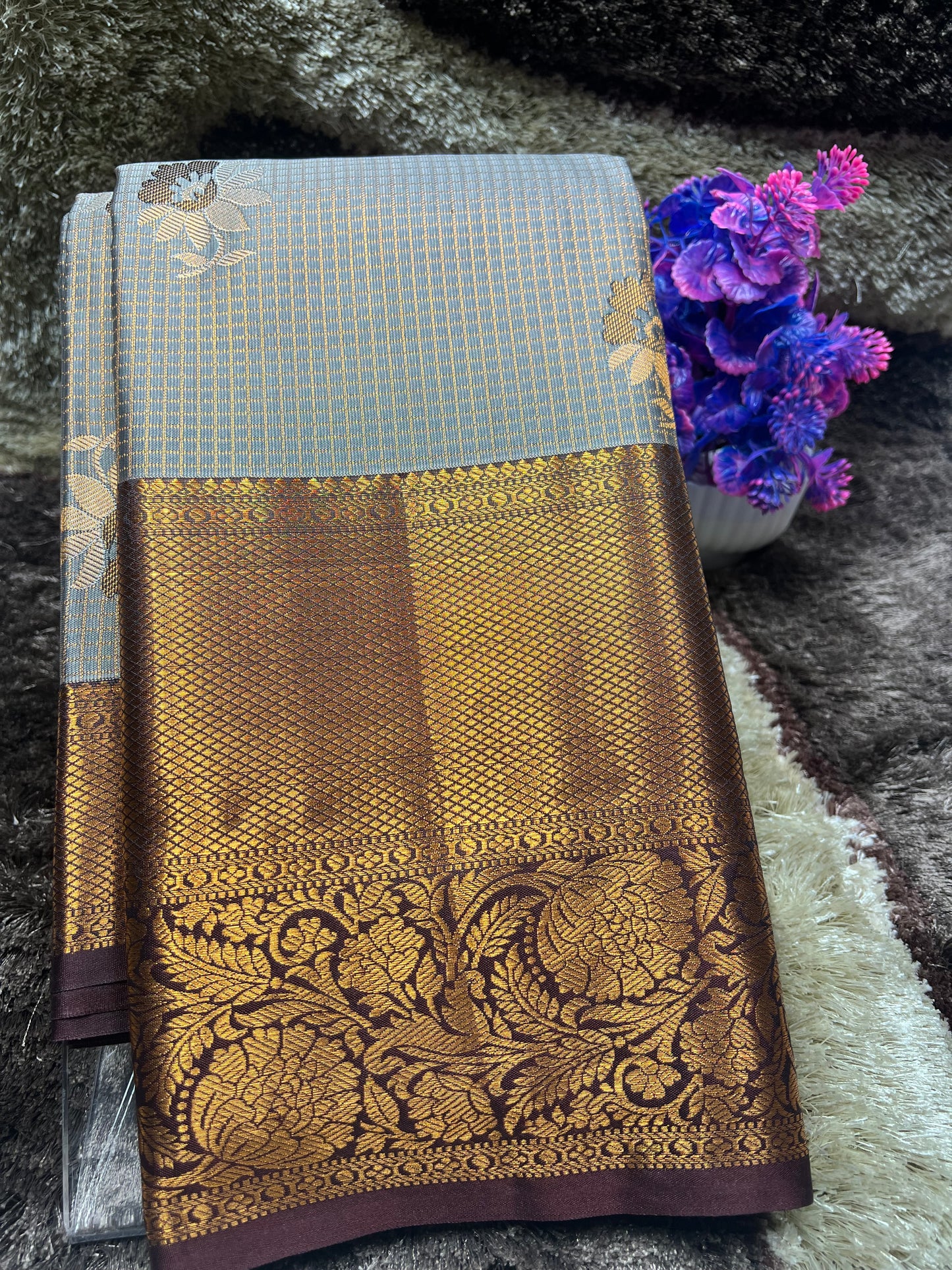 Brown saree with gold patterns on a textured surface with purple flowers.