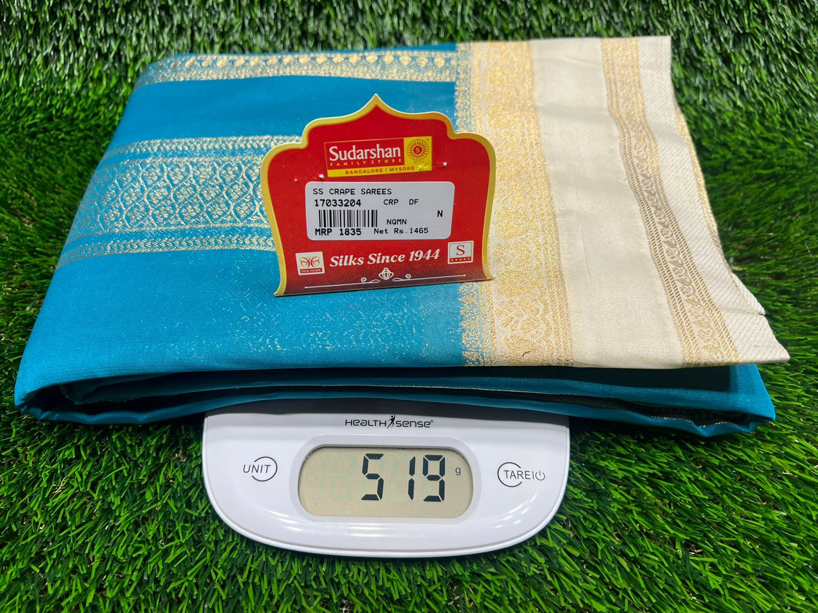 Blue and white fabric with a label on grass, next to a digital scale showing weight.