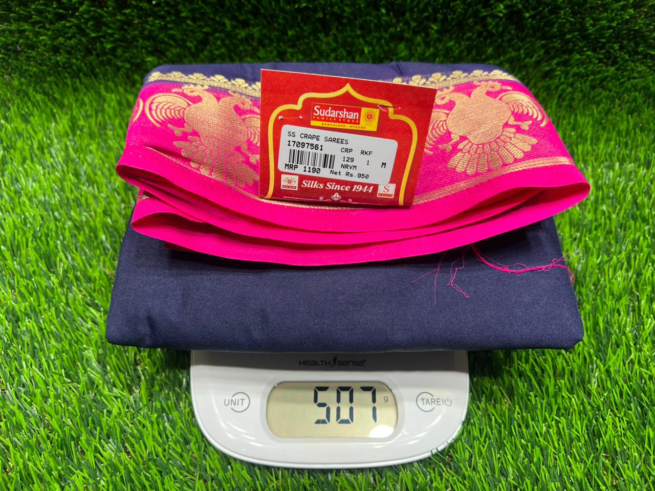 Digital scale with a pink and blue pouch on a green grass background