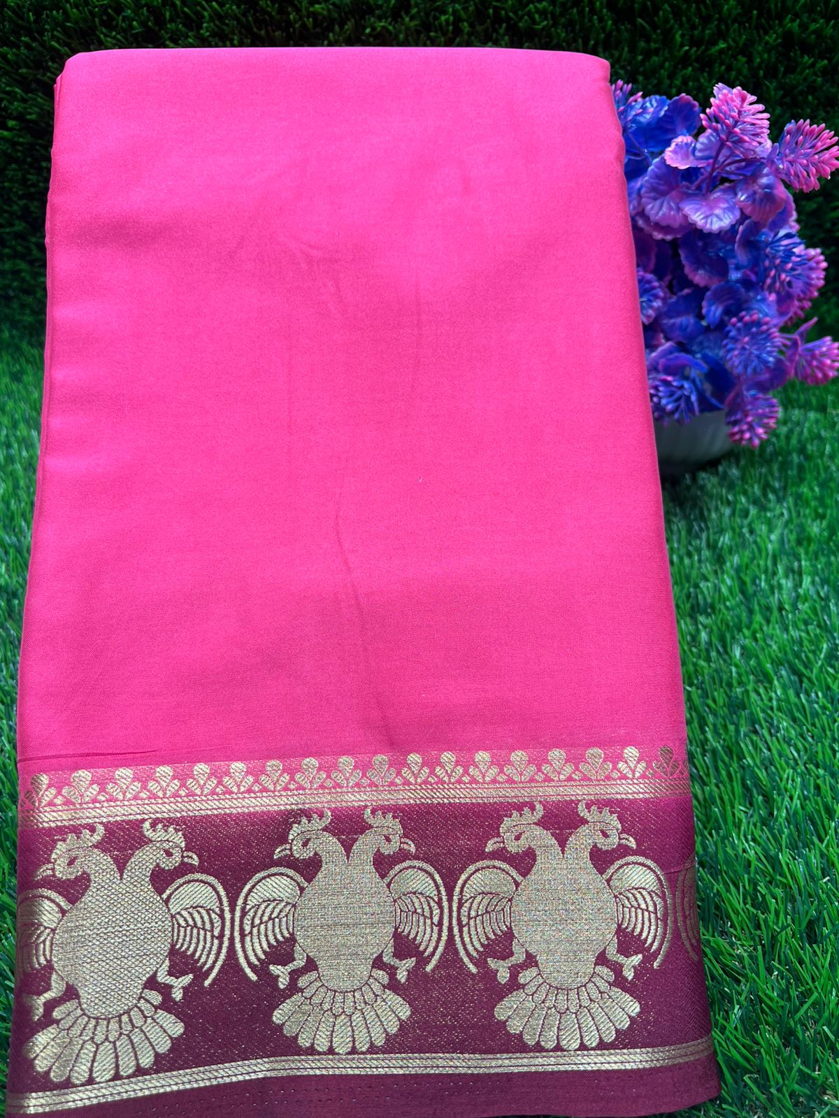 Pink saree with a decorative border on a green grass background