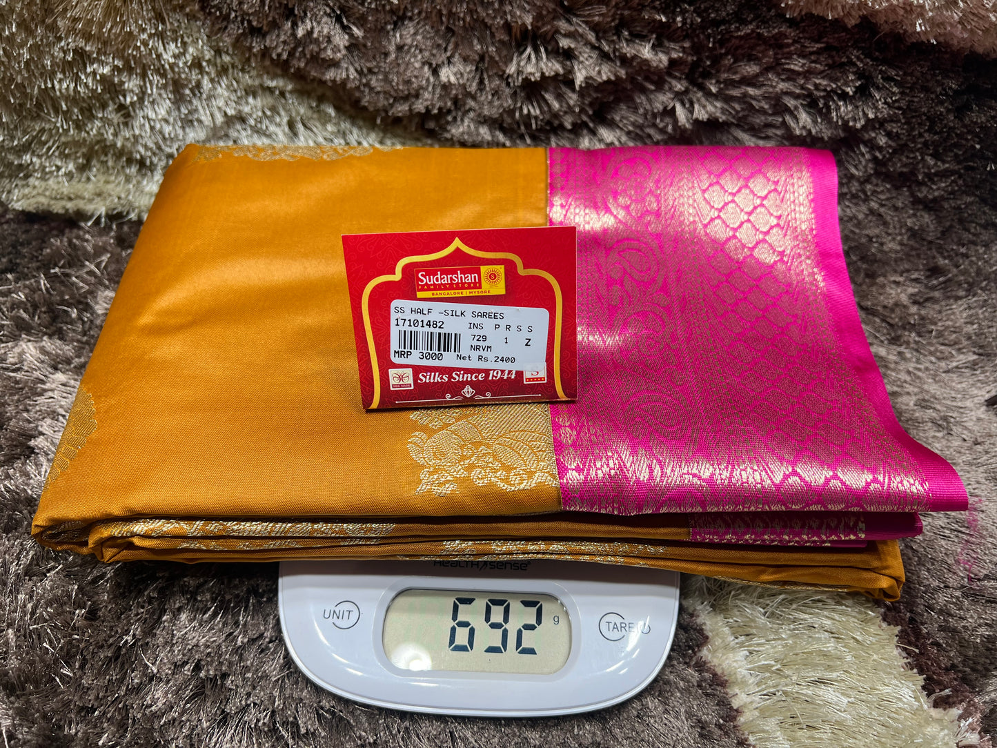 Two fabrics, one gold and one pink with a brand label, on a digital scale.