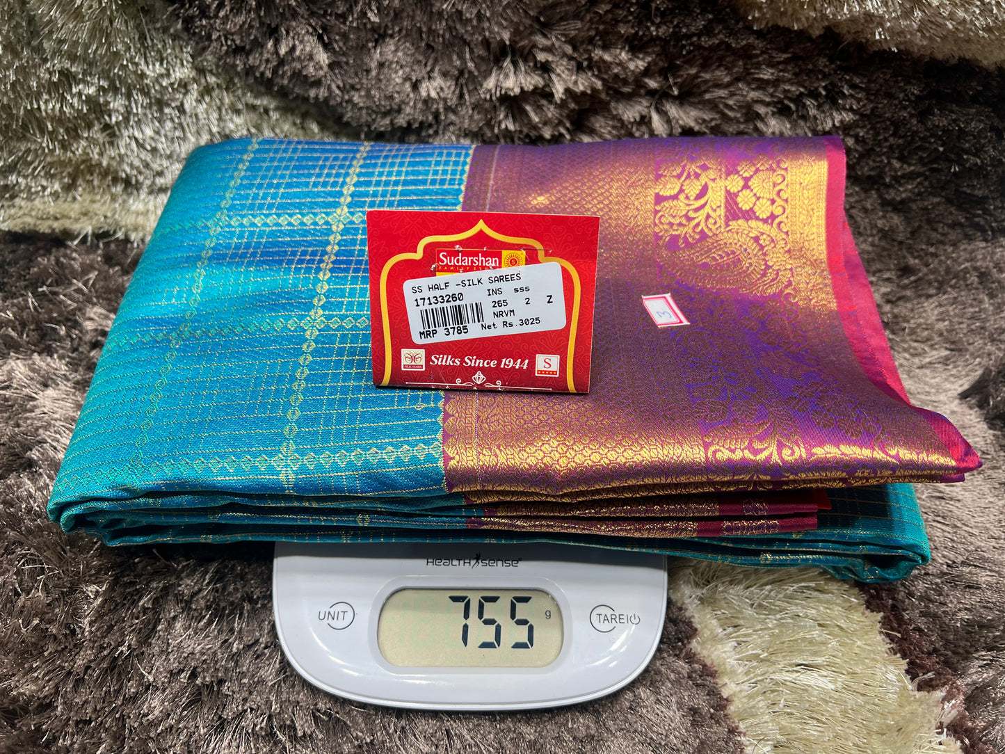 Folded sarees with a scale showing weight on a textured surface