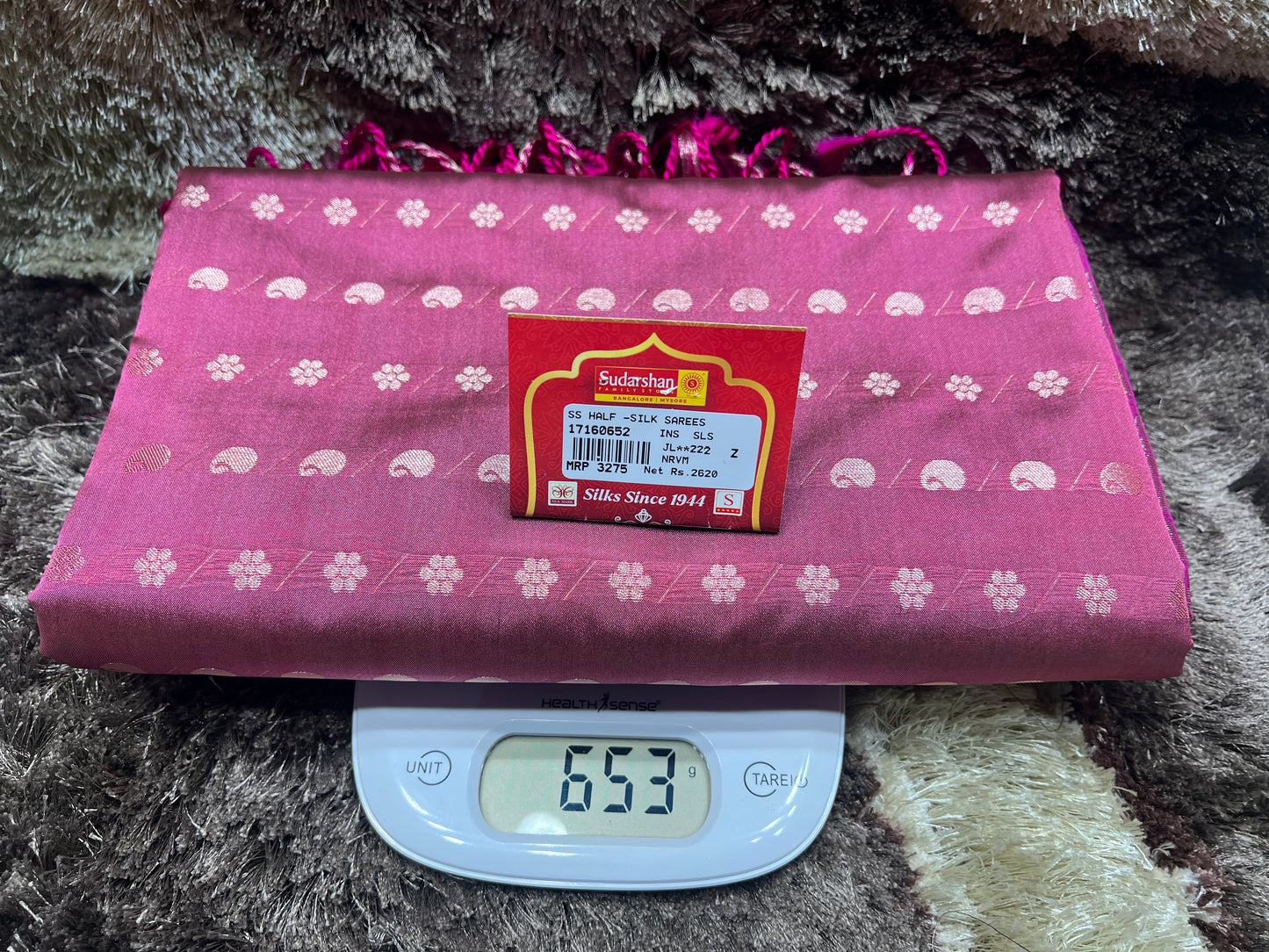 Pink fabric with white patterns on a digital scale displaying weight, against a textured dark background.