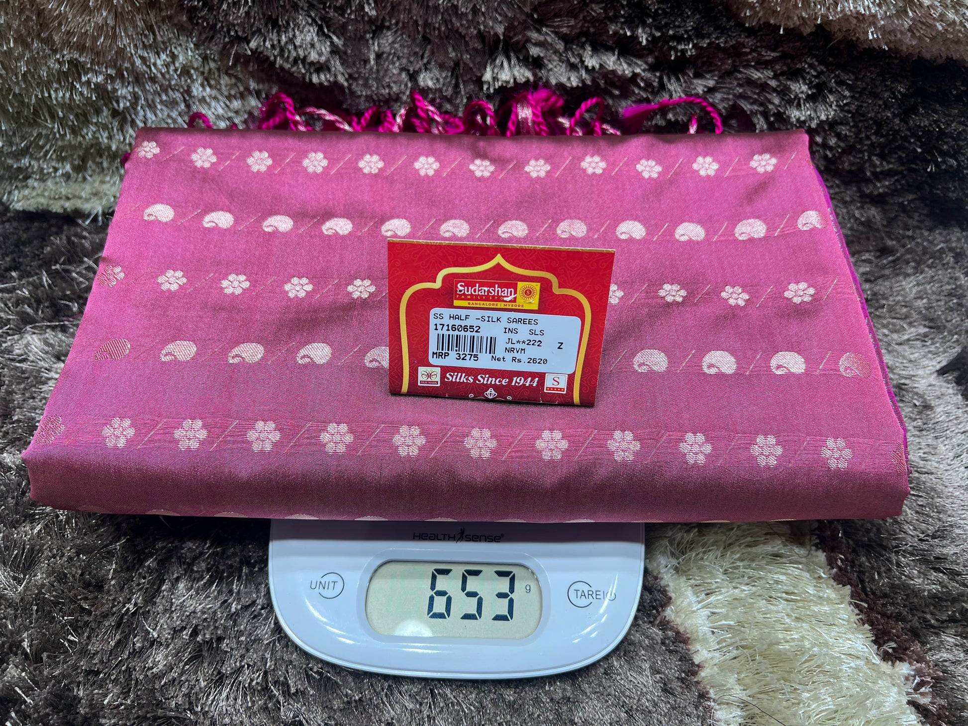 Pink fabric with white patterns on a digital scale displaying weight, against a textured dark background.
