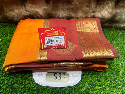 Folded red and orange saree with a label on a digital scale against a grassy background