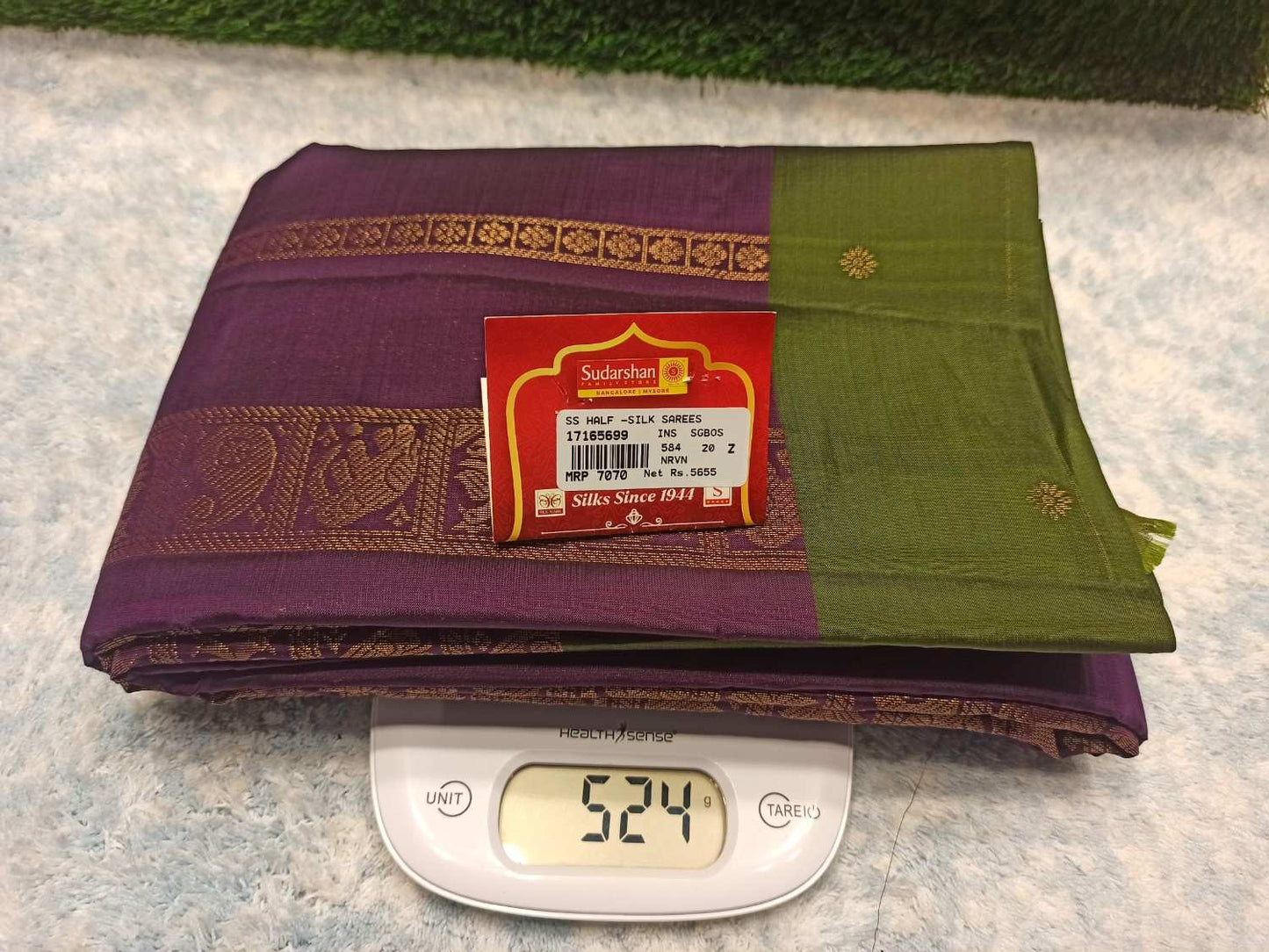 Two sarees, one purple and one green, on a digital scale with a brand label visible.