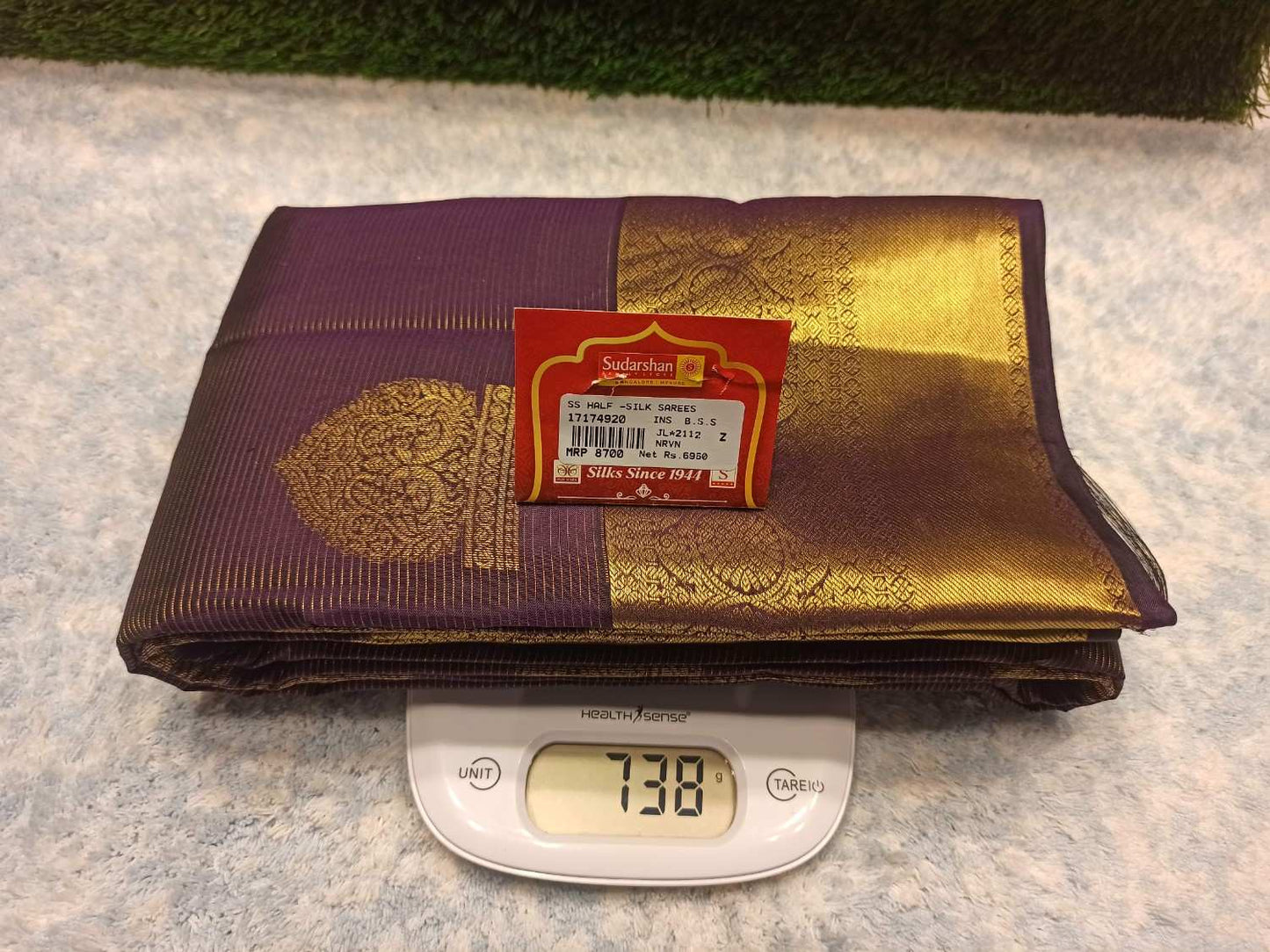 Folded purple and gold fabric with a weight scale displaying 738 grams on a textured surface.
