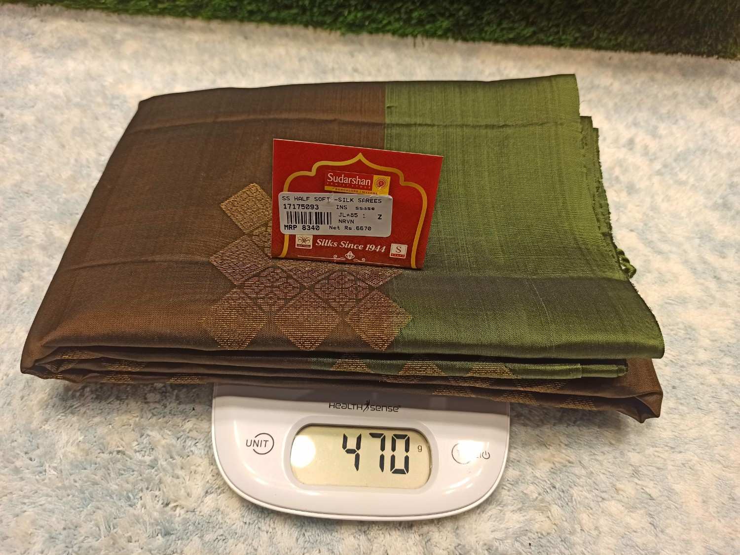Folded brown and green fabric with a label on top of a digital scale showing weight.