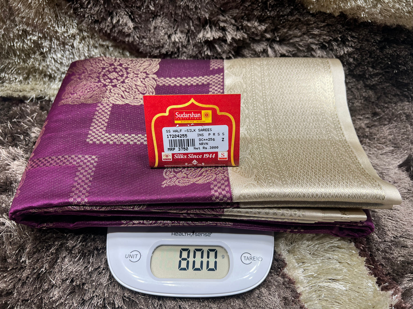 Two fabric swatches, one purple and one gold, with a Sushika label on a digital scale.