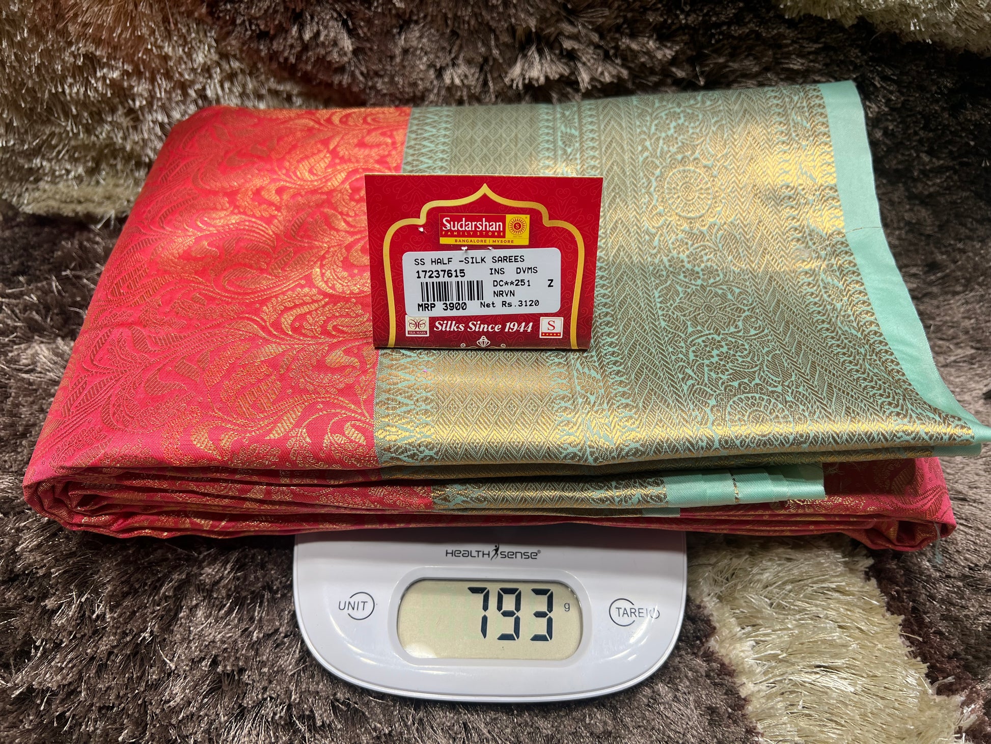 Two folded sarees with a weight scale displaying 793 grams on a textured surface.