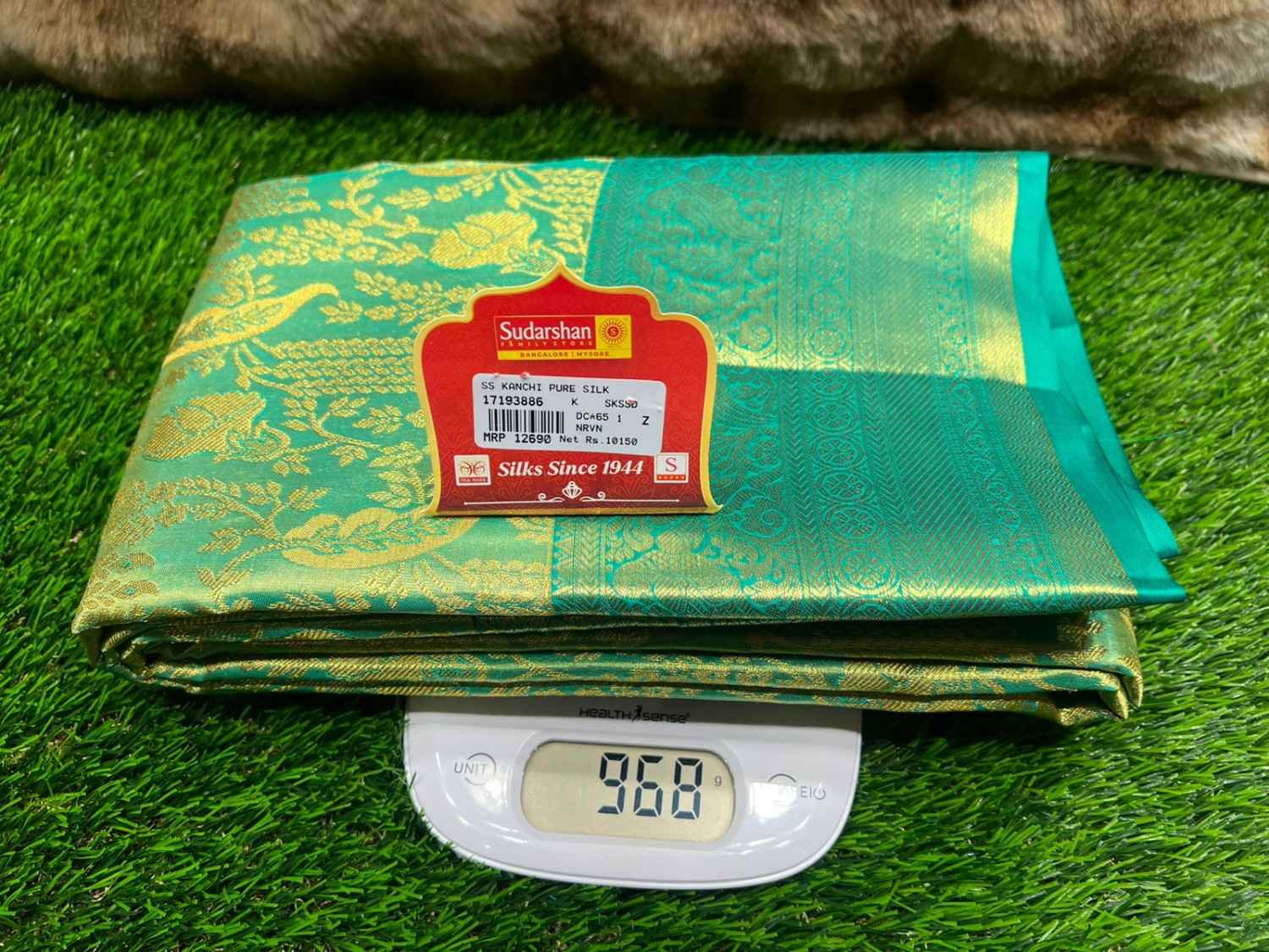 Green fabric with a label on a digital scale displaying weight, placed on green grass.
