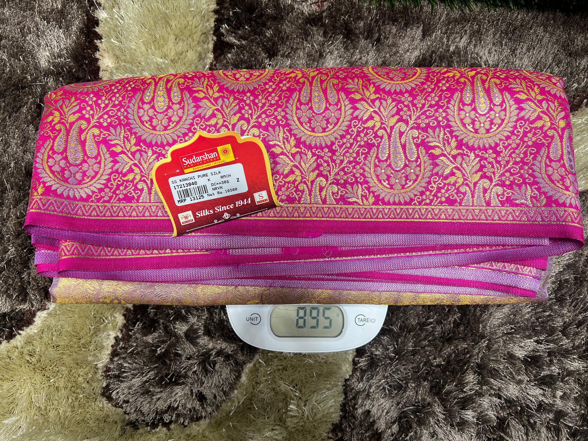 Pink and gold patterned fabric on a digital scale with a brand label.