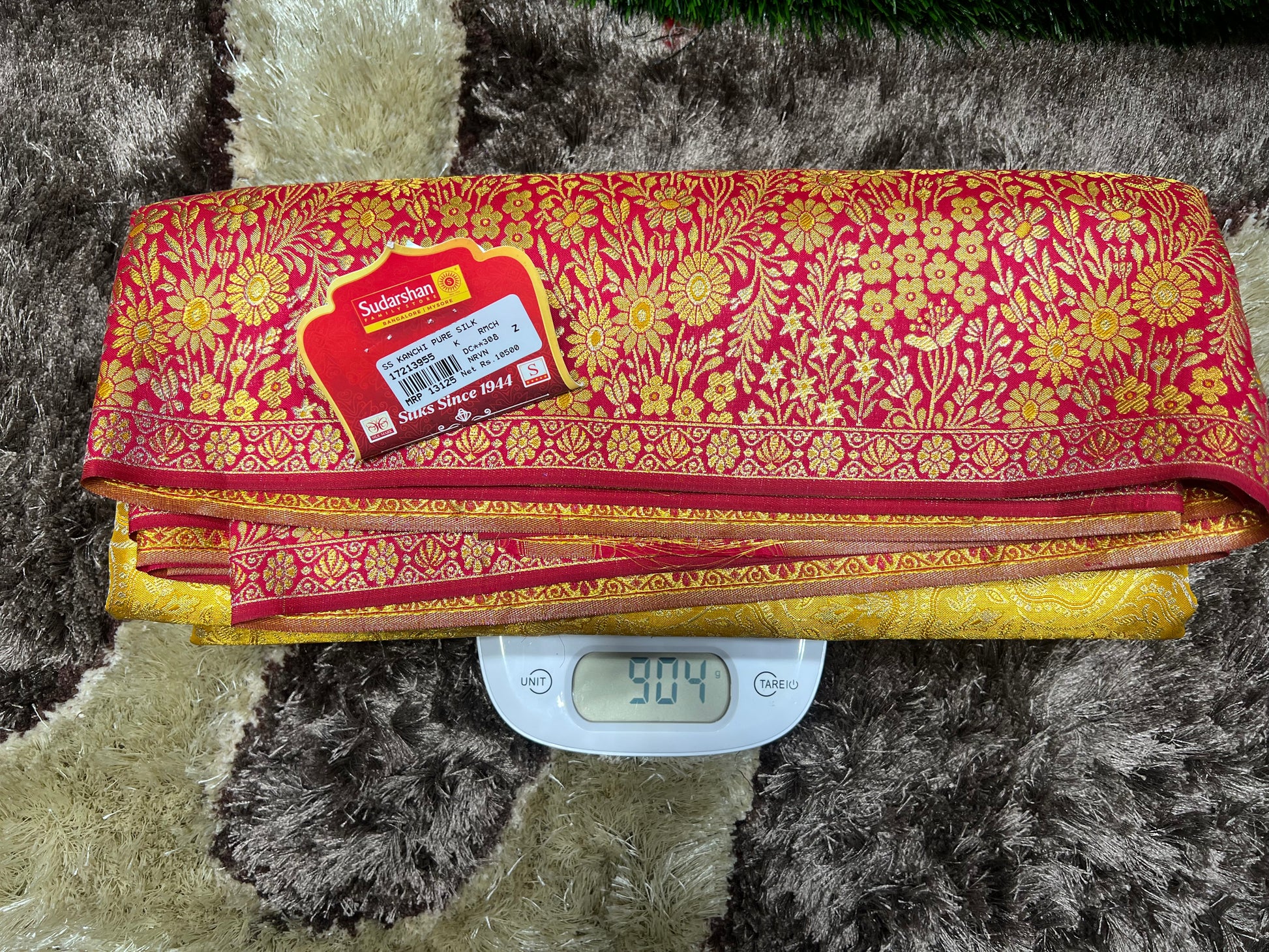 Red and gold patterned fabric on a digital scale with a label on a textured surface