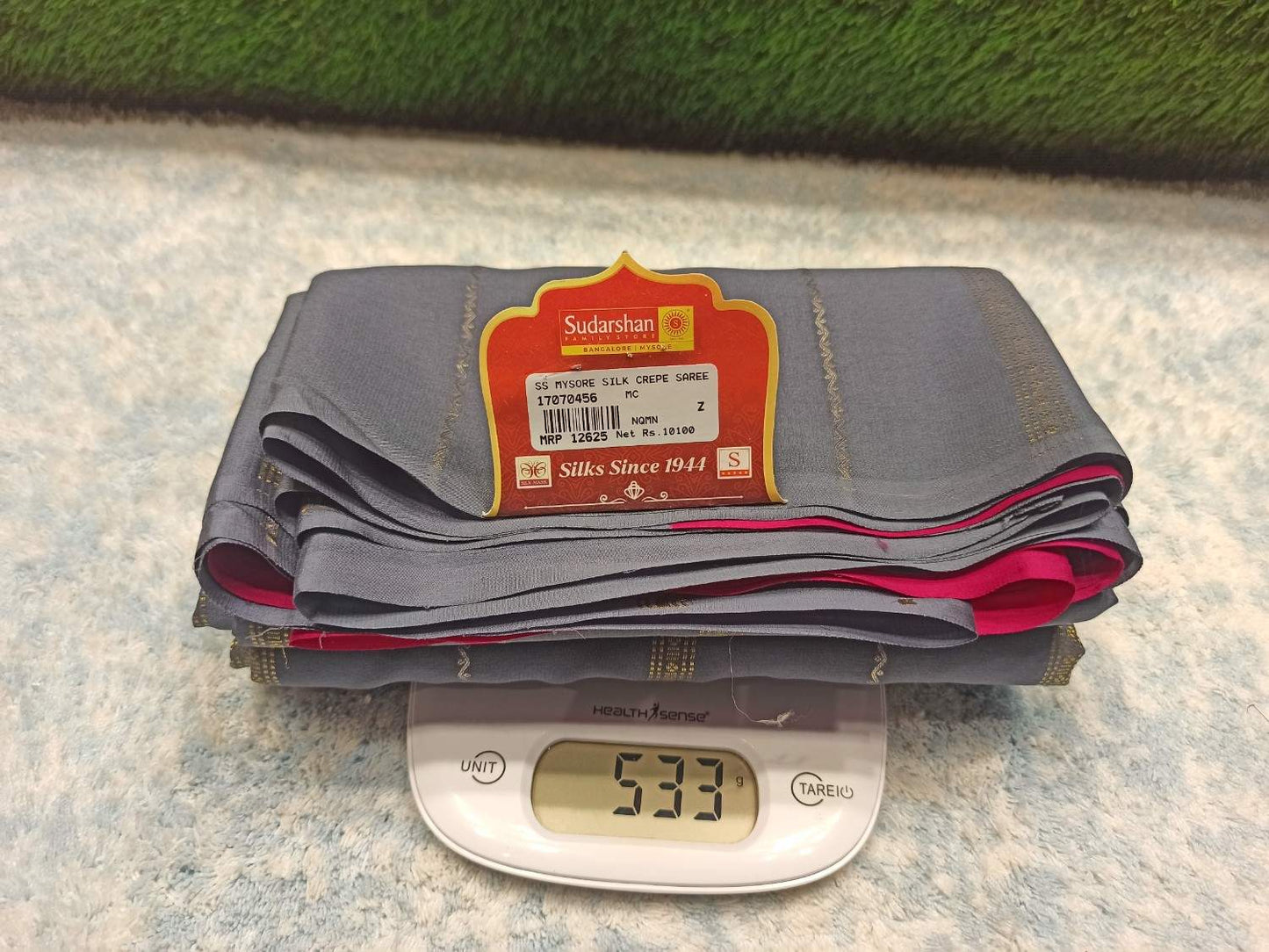 Stack of gray pants with a label on a digital scale showing weight, against a textured surface.