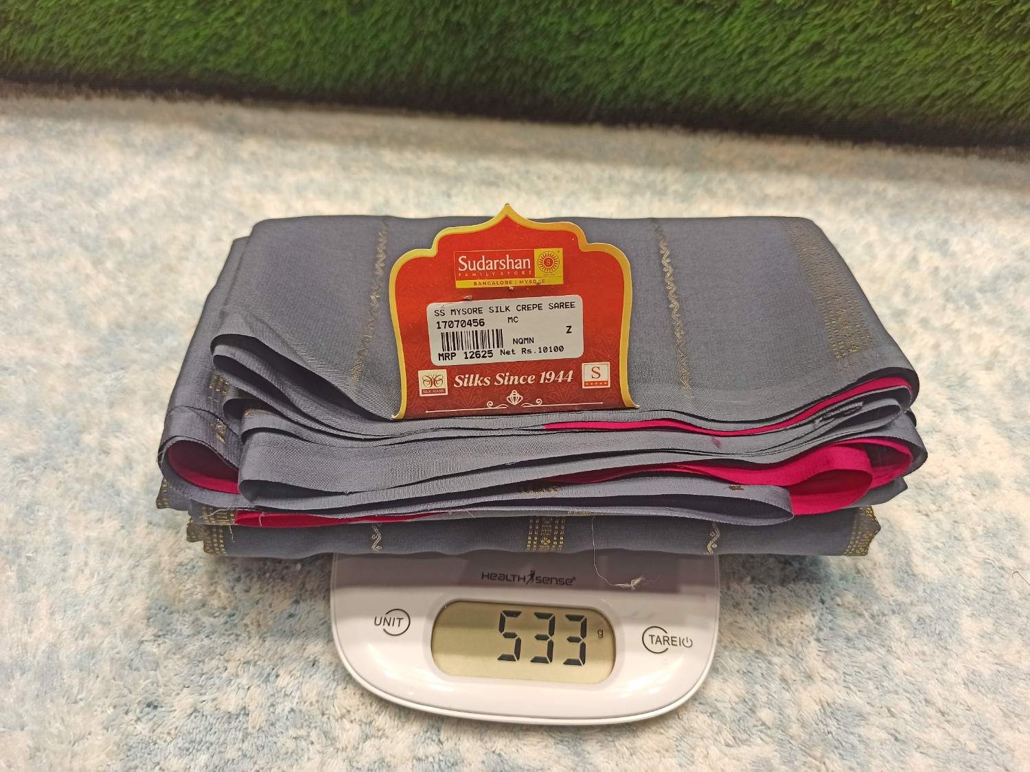Stack of gray pants with a label on a digital scale showing weight, against a textured surface.