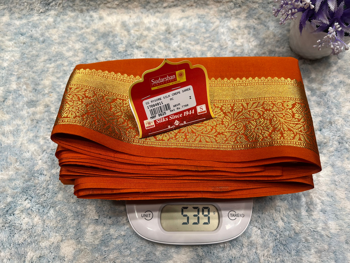 Folded orange fabric with a gold pattern on a digital scale, displaying weight.