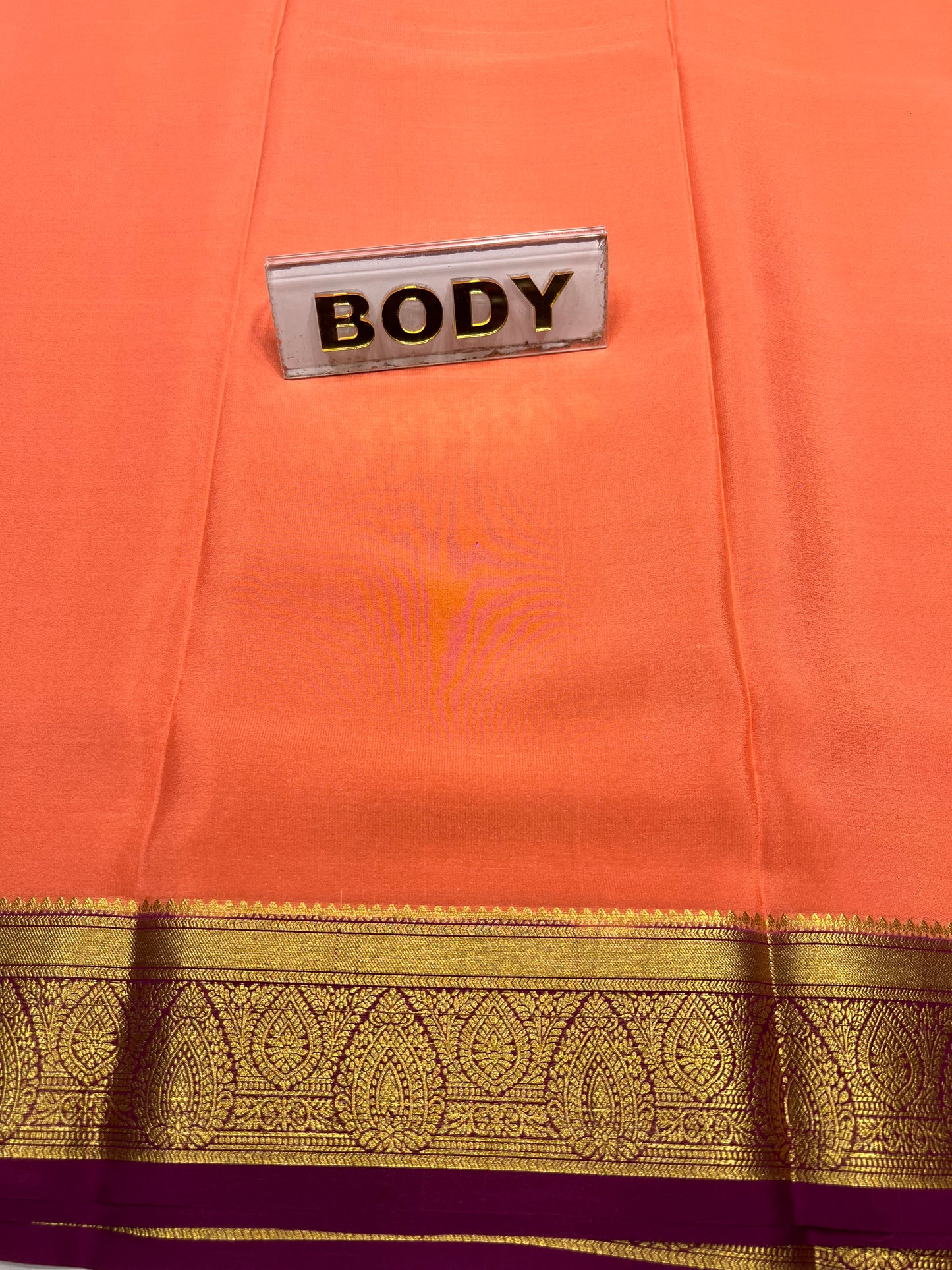 Close-up of an orange saree with a gold border and 'BODY' label.