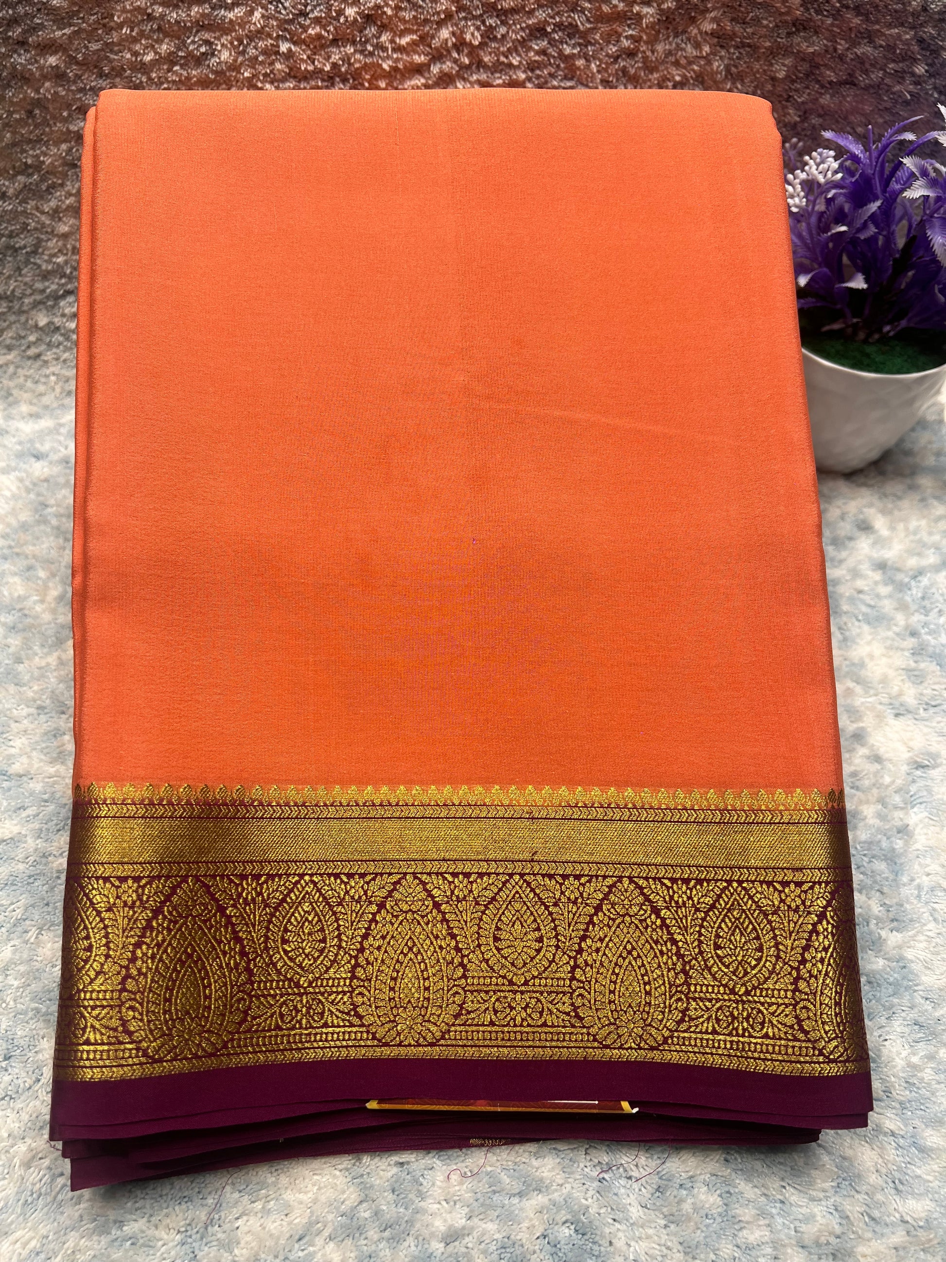 Orange saree with a gold and purple border on a textured surface