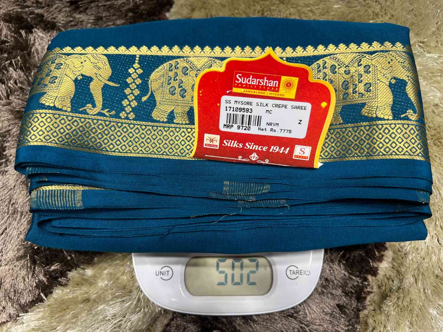 Blue fabric with gold patterns and a Sudarshan label on a digital scale.