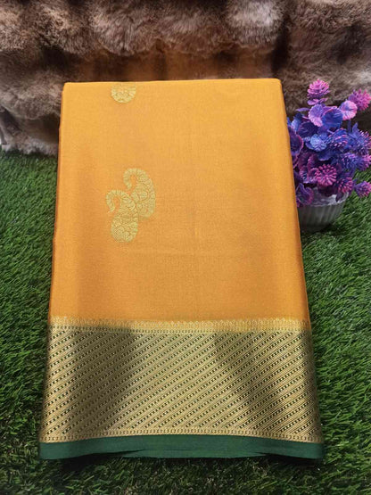 Yellow saree with gold border on a green surface with flowers in the background