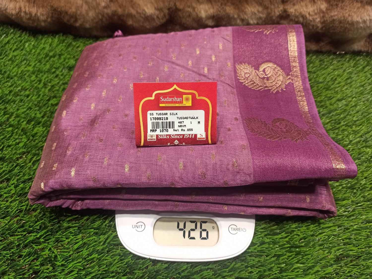 Folded purple fabric with a brand label on a digital scale against a grassy background