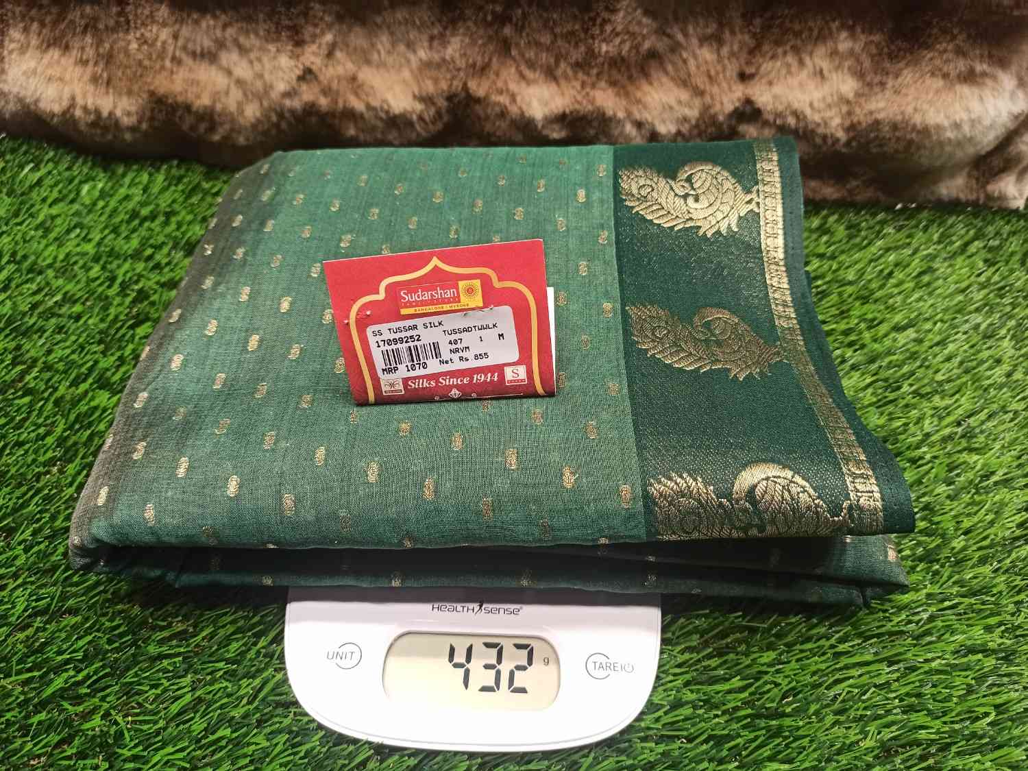 Green fabric with gold patterns on a digital scale, against a green grass-like background