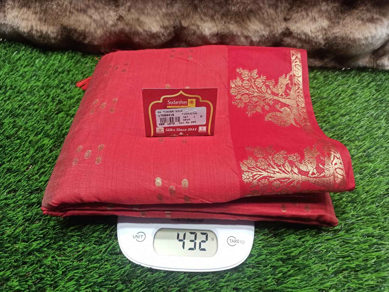 Red fabric with gold patterns on a digital scale against a grass background