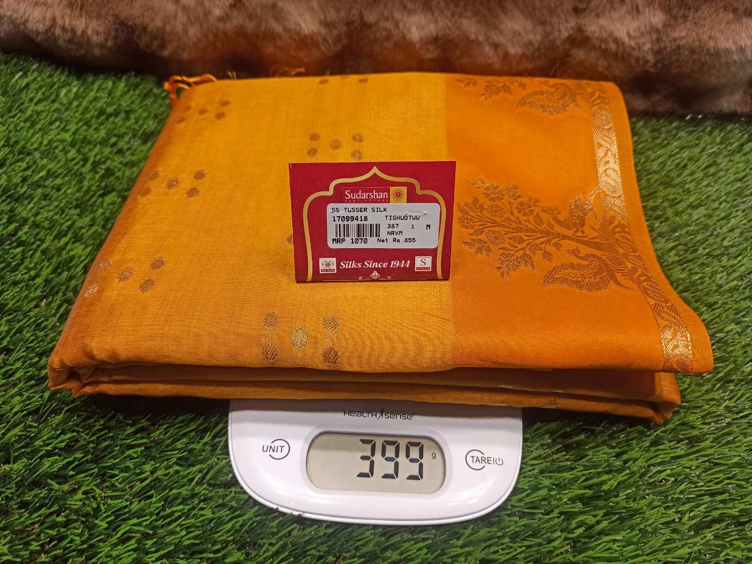 Orange fabric with a label on a digital scale on green grass