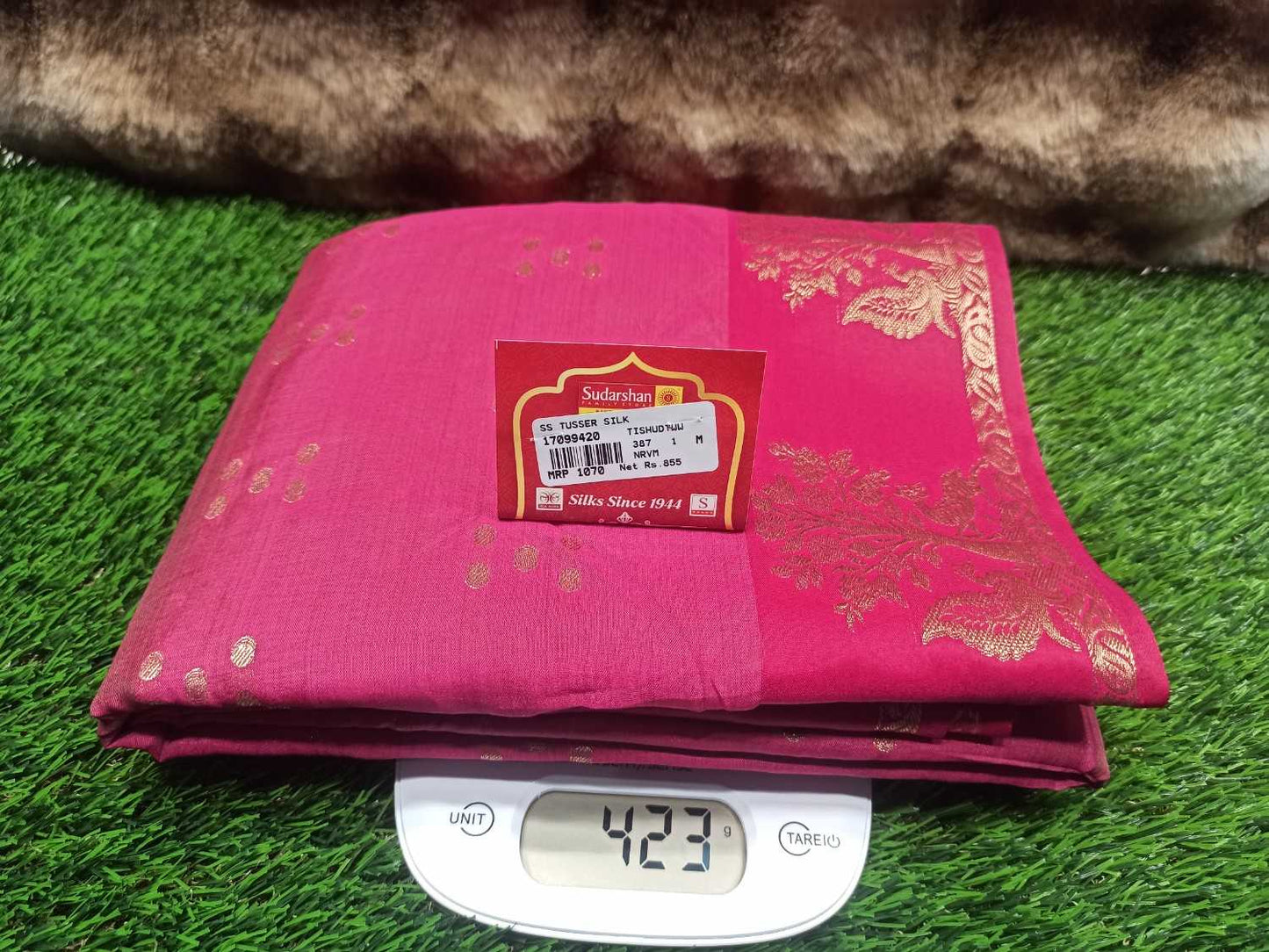 Pink fabric with a label on a digital scale against a grassy background