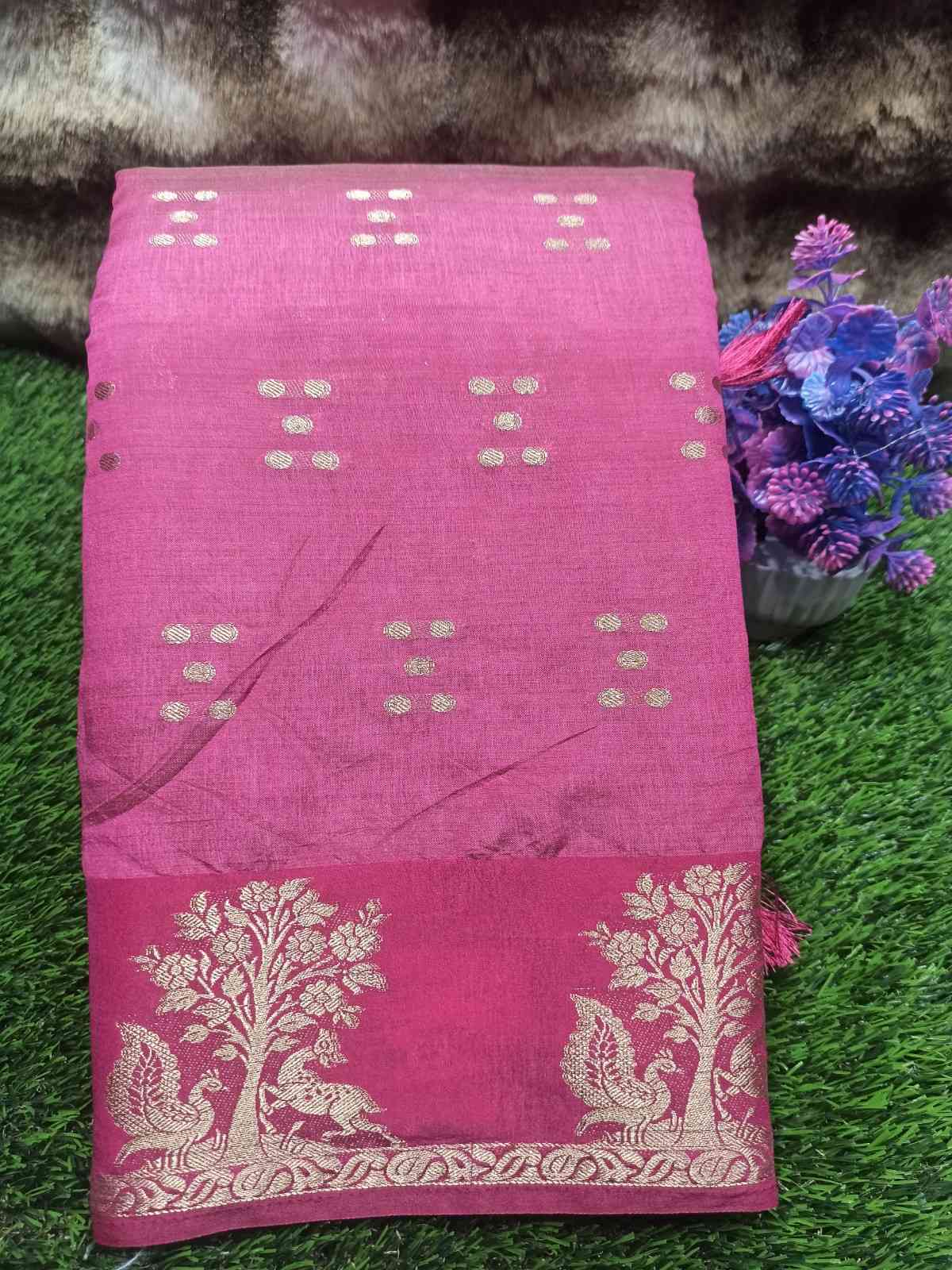 Pink saree with white patterns on a green surface with flowers and fur.
