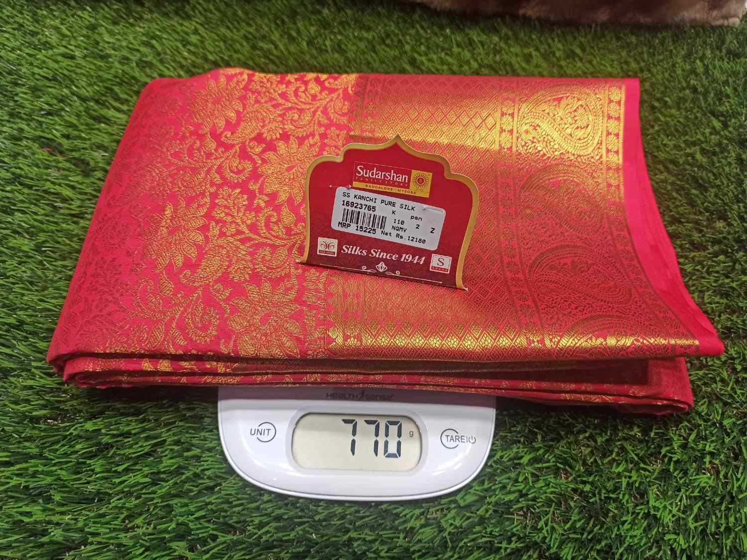 Red and gold saree with a label on a digital scale against a grass background