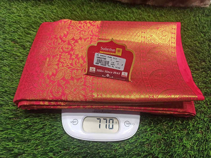 Red and gold saree with a label on a digital scale against a grass background
