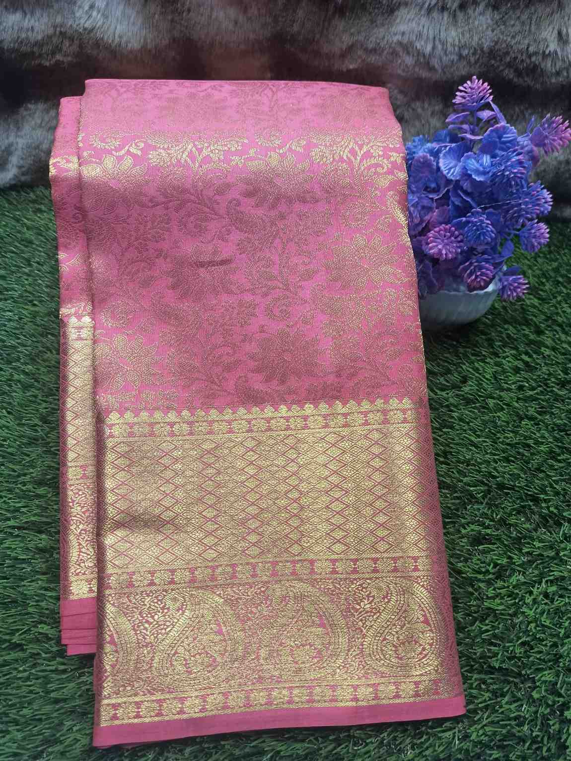 Pink and gold traditional fabric with intricate patterns on a green surface.