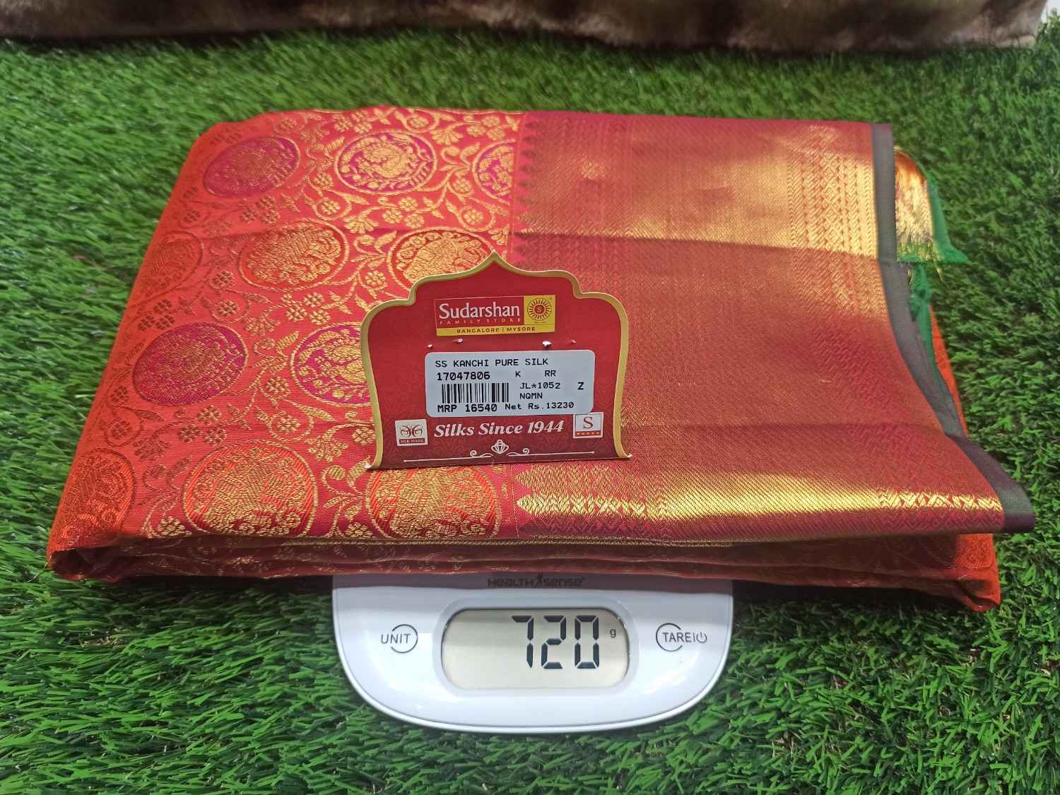 Red saree with gold patterns on a digital scale against a green grass background