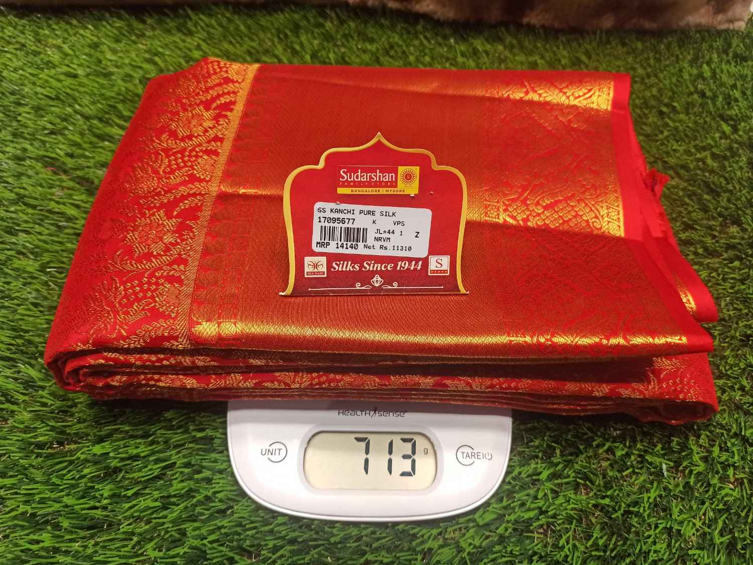 Red saree with gold patterns on a digital scale against a grass background