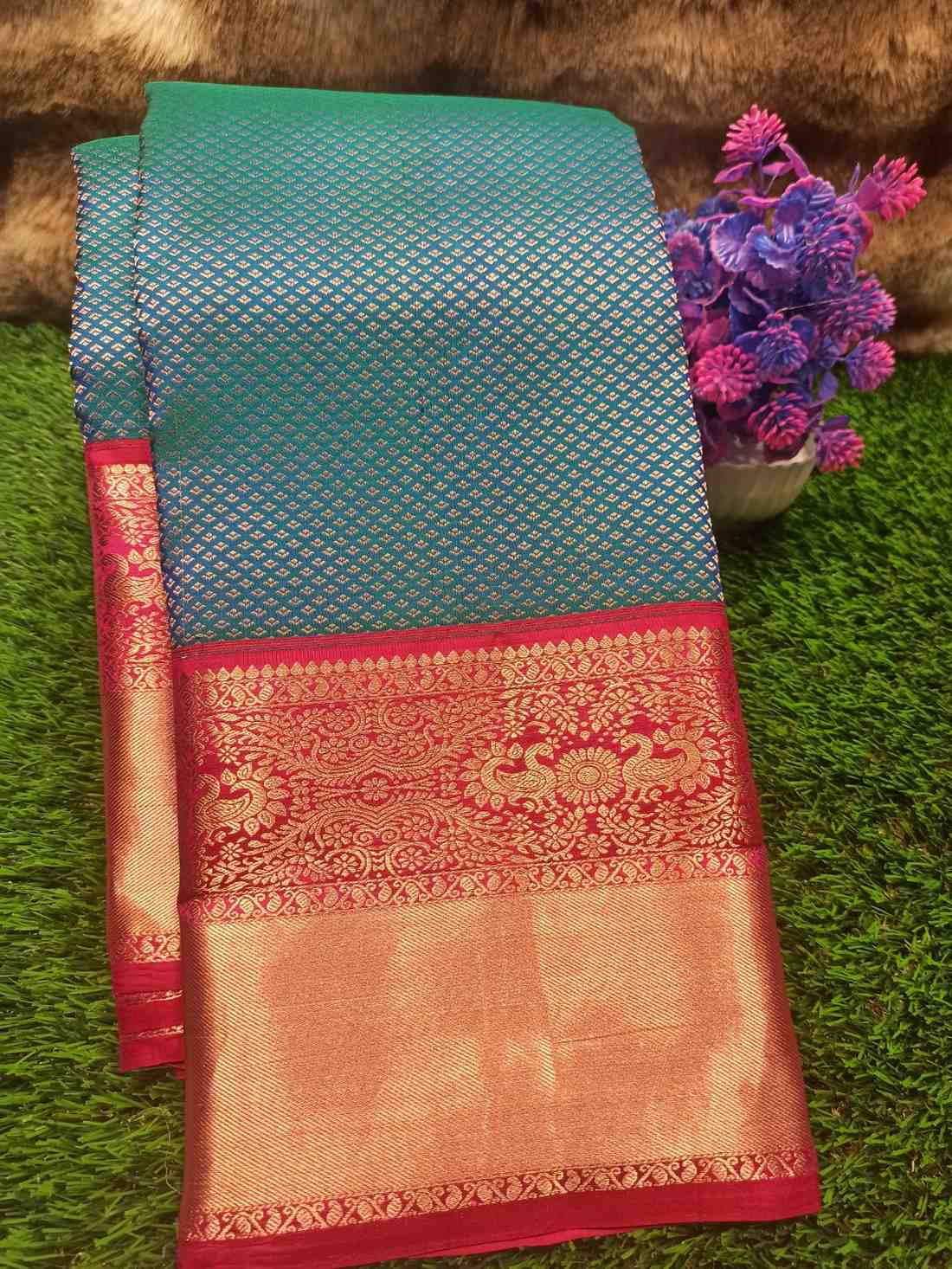 Teal and red saree with floral decoration on a green grass background